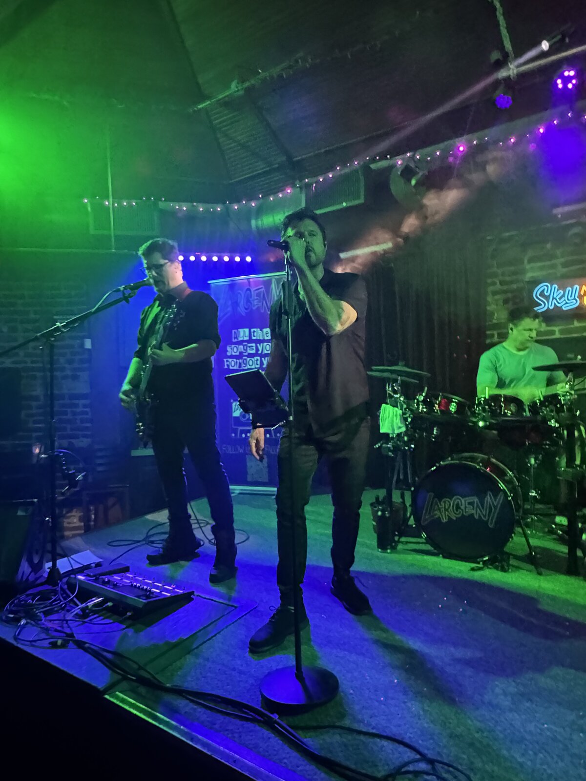 Larceny vocalist Erik singing with rhythm guitarist Dan at Sky Music Lounge with green lighting