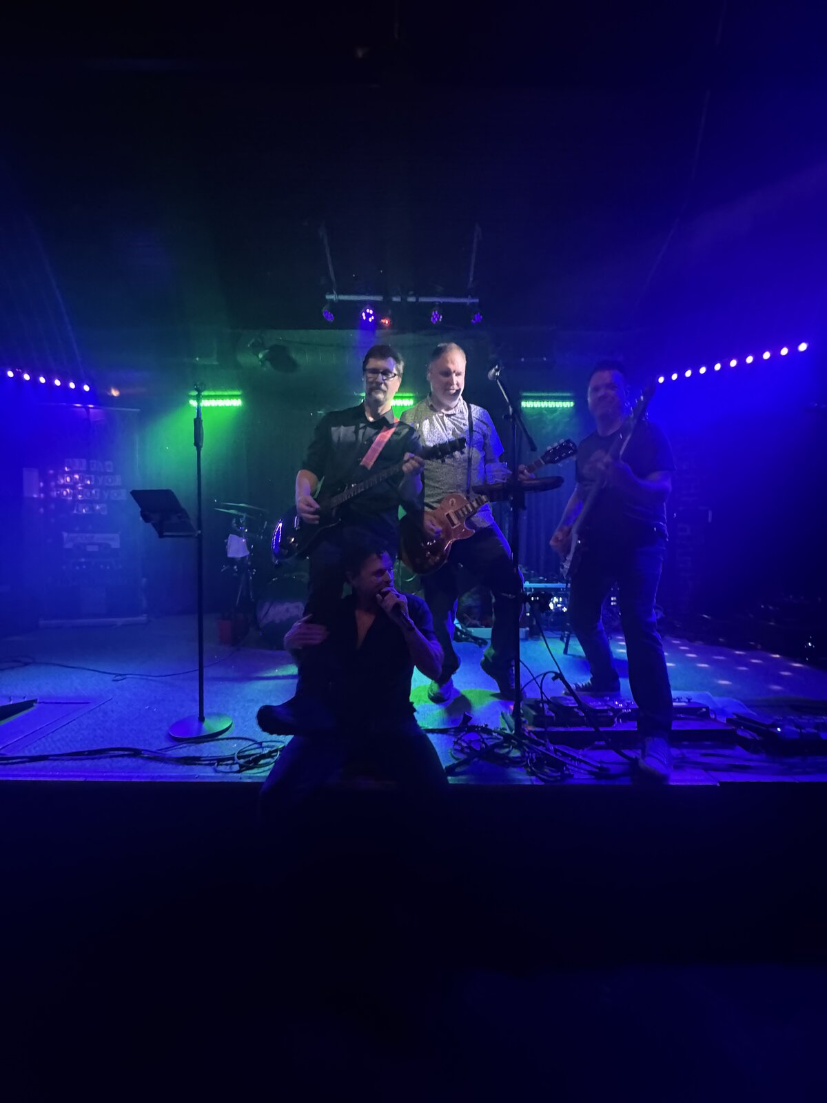 Larceny vocalist Erik kneeling on stage with guitarists Dan and Kevin behind him