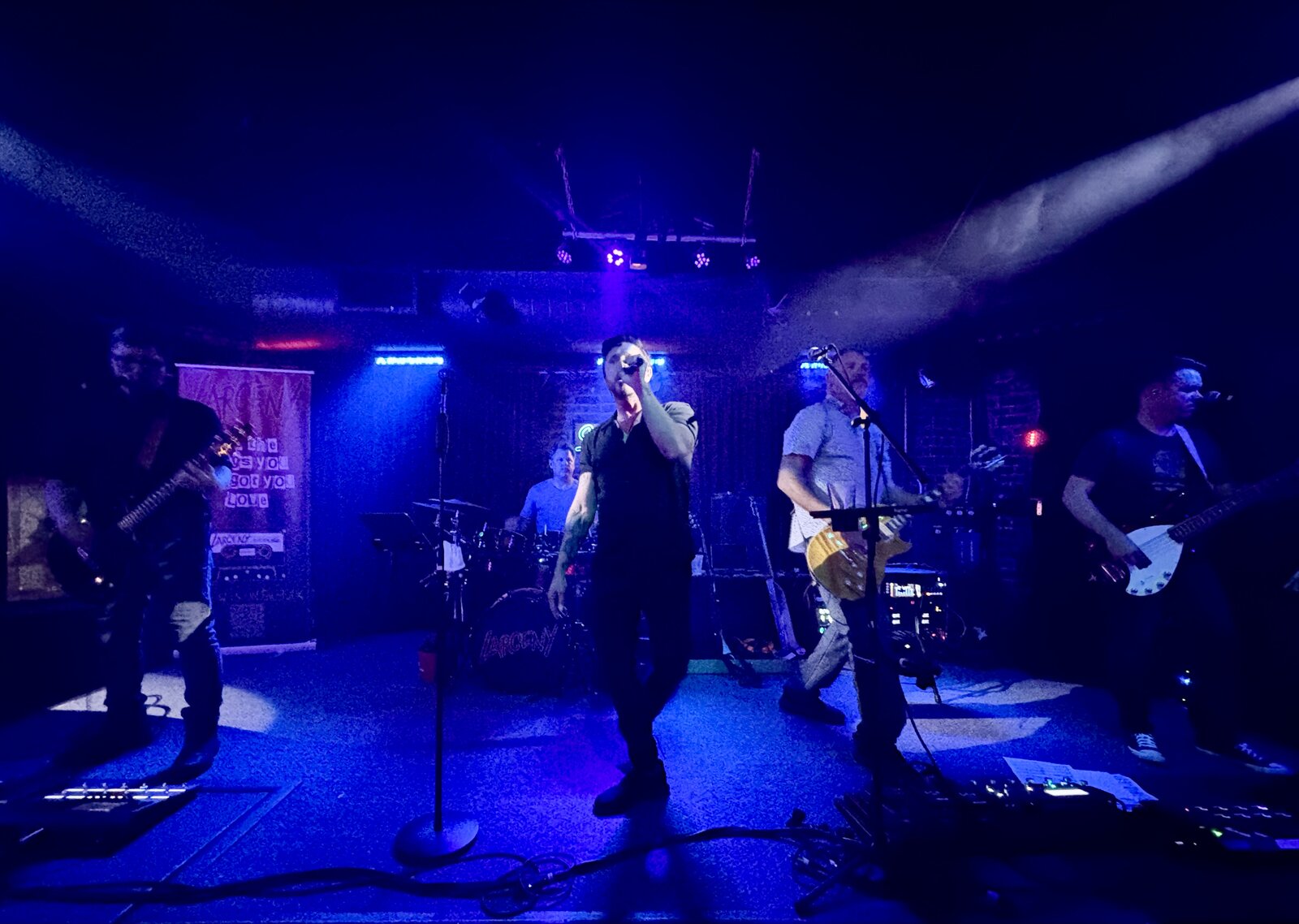 Larceny full band wide shot on stage at Sky Music Lounge with blue lighting and Larceny banner